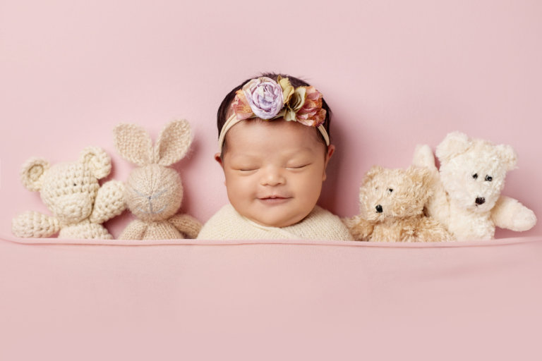 Newborn girl on pink fabric tucked in smiling with animals for girl in Nashua, New Hampshire